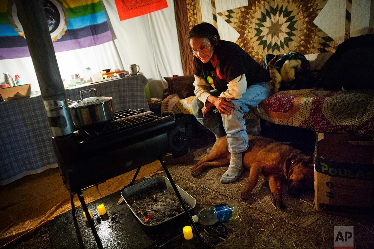 In this Tuesday, Nov. 29, 2016 photo, Grandma Redfeather of the Sioux Native American tribe sits by the wood stove in her yurt at the Oceti Sakowin camp where people have gathered to protest the Dakota Access oil pipeline in Cannon Ball, N.D. "I love it because I get to live my traditional way of life," said Redfeather of living at the camp. "To see all the different tribal nations living together as a community, I would have loved my grandpa to see that." (AP Photo/David Goldman)