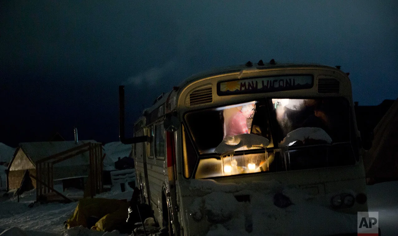 In this Wednesday, Nov. 30, 2016 photo, a person is seen inside a bus turned into a camper at the Oceti Sakowin camp where people have gathered to protest the Dakota Access pipeline near Cannon Ball, N.D. The camp covers a half square mile, with living quarters that include old school buses, fancy motorhomes and domelike yurts. Hay bales are piled around some teepees to keep out the wind. There's even a crude corral for horses. (AP Photo/David Goldman)