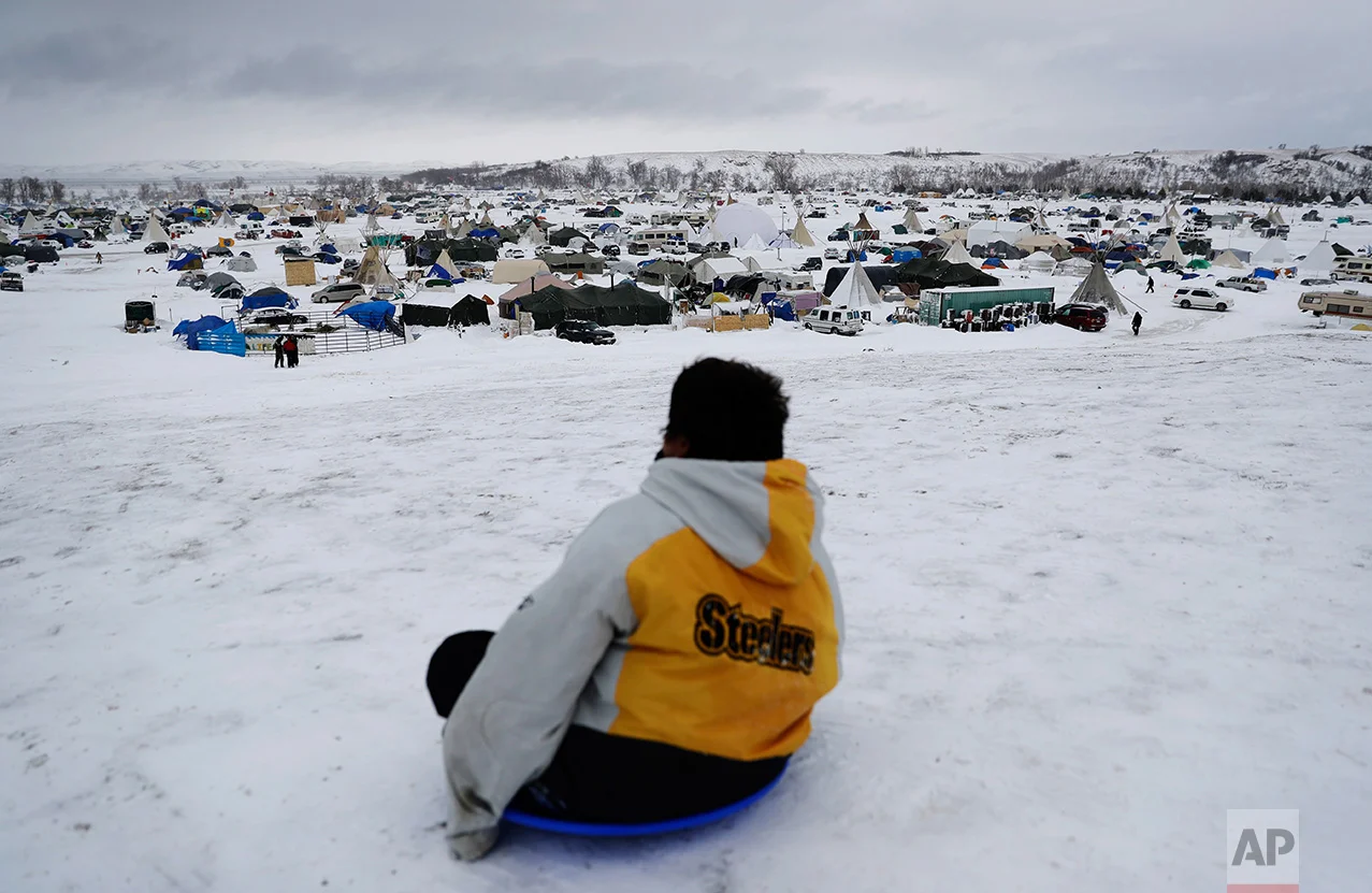 In this Tuesday, Nov. 29, 2016 photo, the Oceti Sakowin camp where people have gathered to protest the Dakota Access oil pipeline stands in the background as a boy sleds down a hill in Cannon Ball, N.D. The government has ordered protesters to leave federal land by Monday, but they insist they will stay for as long it takes to divert the $3.8 billion pipeline. (AP Photo/David Goldman)