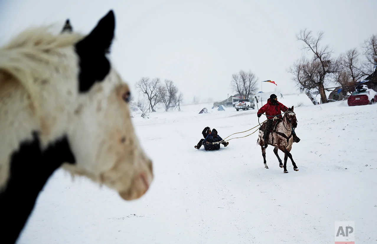 In this Tuesday, Nov. 29, 2016 photo, Smokey, a member of the Sioux Native American tribe, rides the horse Prophecy, a descendant of the horse belonging to war chief Crazy Horse, as he pulls a sled at the Oceti Sakowin camp where people have gathered to protest the Dakota Access oil pipeline, in Cannon Ball, N.D. The government has ordered protesters to leave federal land by Monday, but they insist they will stay for as long it takes to divert the $3.8 billion pipeline. (AP Photo/David Goldman)