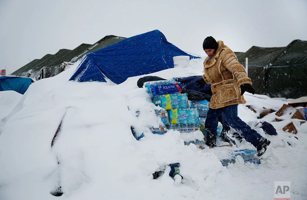 In this Tuesday, Nov. 29, 2016 photo, Lawrence Valdez, of New Mexico and a member of the Chiricahua Apache Native American tribe, drops off bottles of water at the Oceti Sakowin camp where people have gathered to protest the Dakota Access oil pipeline, in Cannon Ball, N.D. Camp dwellers are getting ready for the hardships of a long stay. Mountains of donated food and water are being stockpiled, as is firewood, much of which has come from outside of North Dakota, the least-forested state in the nation. (AP Photo/David Goldman)