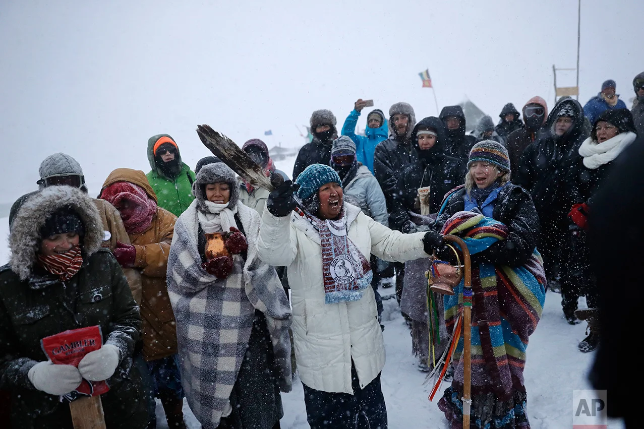 In this Tuesday, Nov. 29, 2016 photo, Beatrice Menase Kwe Jackson of the Ojibwe Native American tribe leads a song during a traditional water ceremony along the Cannonball river at the Oceti Sakowin camp where people have gathered to protest the Dakota Access oil pipeline in Cannon Ball, N.D. The pipeline is largely complete except for a short segment that is planned to pass beneath a Missouri River reservoir. The company doing the building says it is unwilling to reroute the project. (AP Photo/David Goldman)