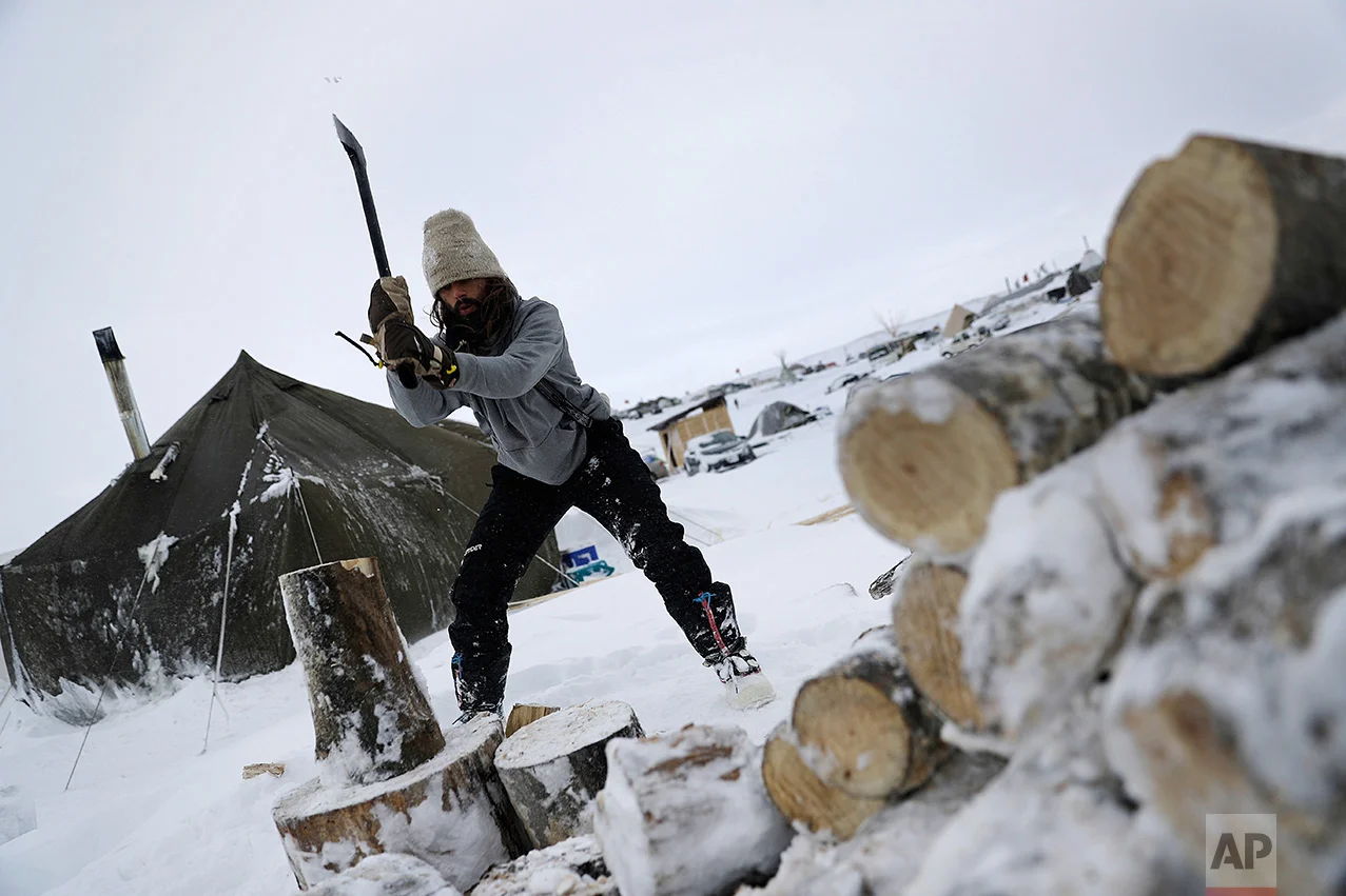 In this Tuesday, Nov. 29, 2016 photo, Blackhorse Shasta, of Oregon, chops wood on the Oceti Sakowin camp where people have gathered to protest the Dakota Access pipeline near Cannon Ball, N.D. Camp dwellers are getting ready for the hardships of a long stay. Mountains of donated food and water are being stockpiled, as is firewood, much of which has come from outside of North Dakota, the least-forested state in the nation. (AP Photo/David Goldman)