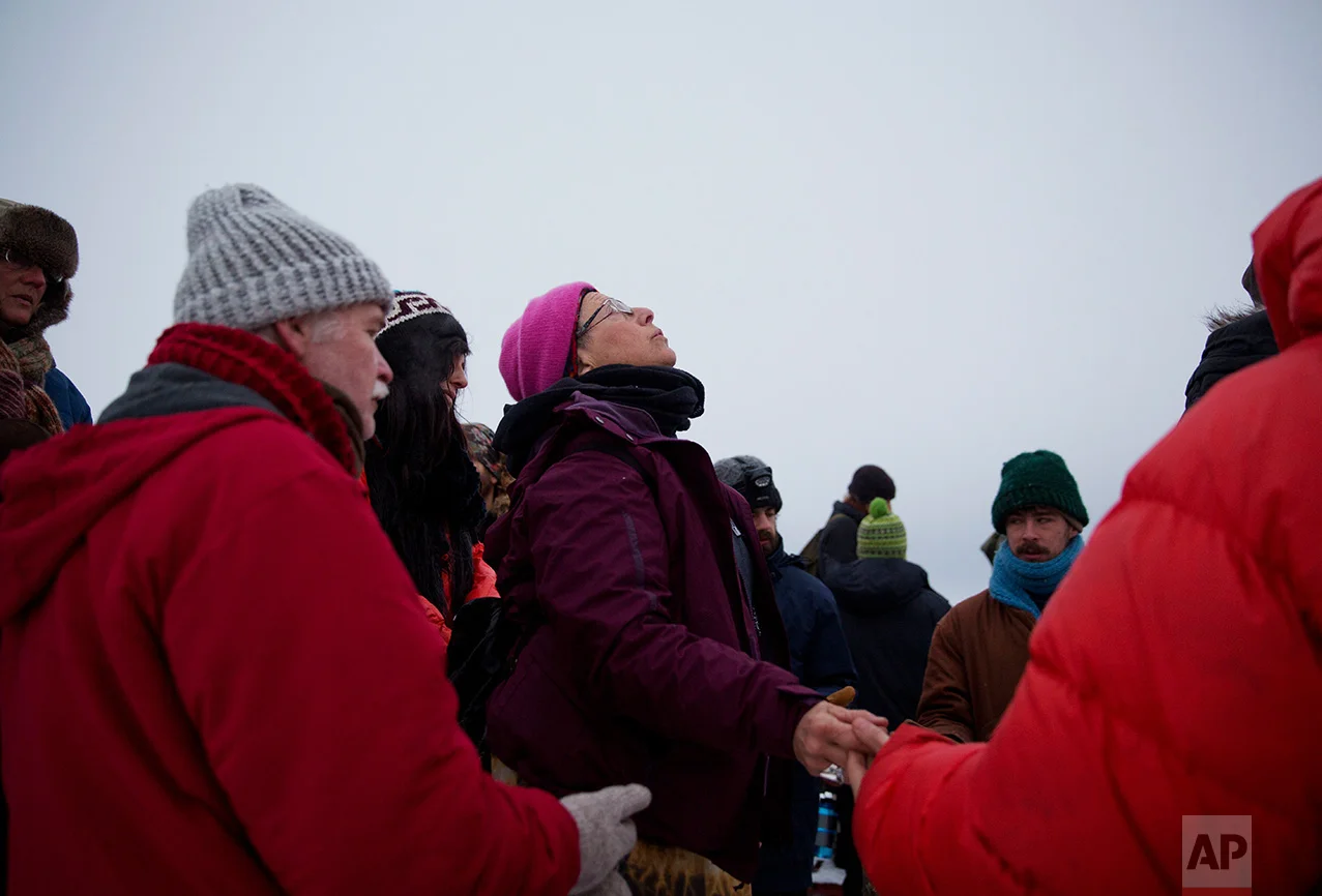 In this Thursday, Dec. 1, 2016 photo, Elena Ruben Goodman, of Oakland, Calif., waits her turn to pray by the Cannonball river during a Native American water ceremony at the Oceti Sakowin camp where people have gathered to protest the Dakota Access oil pipeline in Cannon Ball, N.D. On Thursday, the camp near the confluence of the Missouri and Cannonball rivers was shrouded in snow, much of it compacted by foot and vehicle traffic. Next week's forecast calls for single digits and subzero wind chills. (AP Photo/David Goldman)