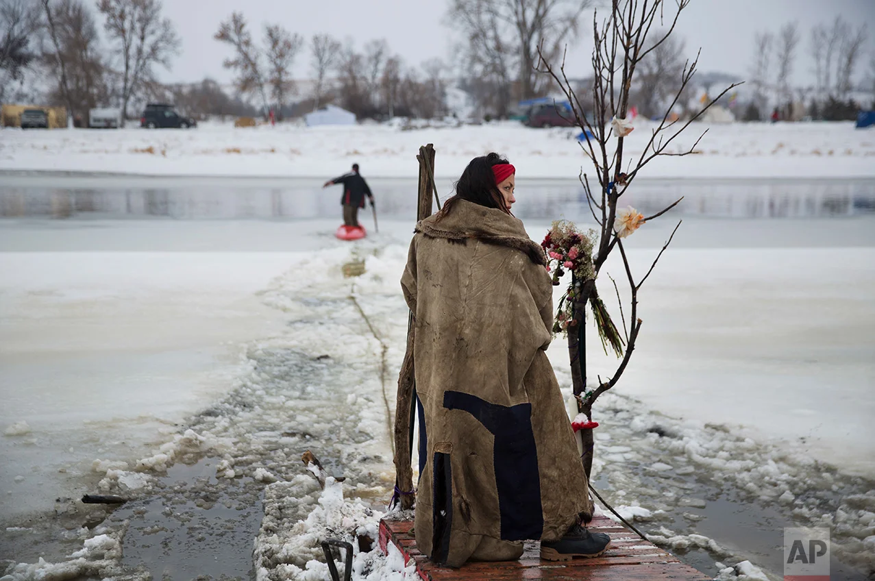 In this Thursday, Dec. 1, 2016 photo, Cat Bigney, part of the Oglala Native American tribe, waits on the shore of the Cannonball river for travelers to arrive by canoe at the Oceti Sakowin camp where people have gathered to protest the Dakota Access oil pipeline in Cannon Ball, N.D. So far, those at the camp have shrugged off the heavy snow, icy winds and frigid temperatures. But if they defy next week's government deadline to abandon the camp, demonstrators know the real deep freeze lies ahead. Life-threatening wind chills and towering snow drifts could mean the greatest challenge is simple survival. (AP Photo/David Goldman)