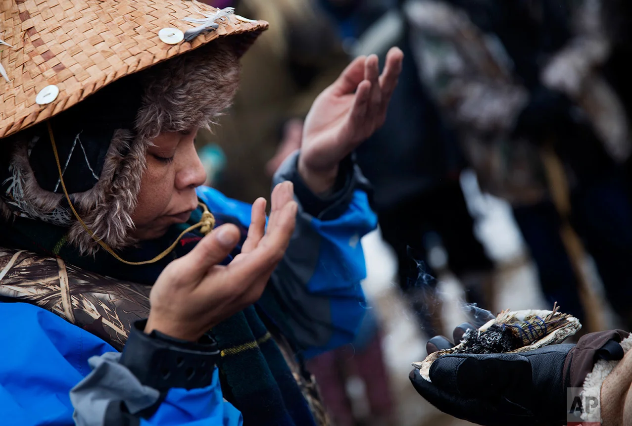 In this Thursday, Dec. 1, 2016 photo, Virginia Redstar of Colville, Wash., and a member of the Colville Native American tribe, allows smoke from burning sage wash over her during a ritual after reaching shore by canoe at the Oceti Sakowin camp where people have gathered to protest the Dakota Access oil pipeline in Cannon Ball, N.D. Redstar traveled from Montana with fellow tribal members on canoe for 10 days down the Missouri river to reach the camp. (AP Photo/David Goldman)