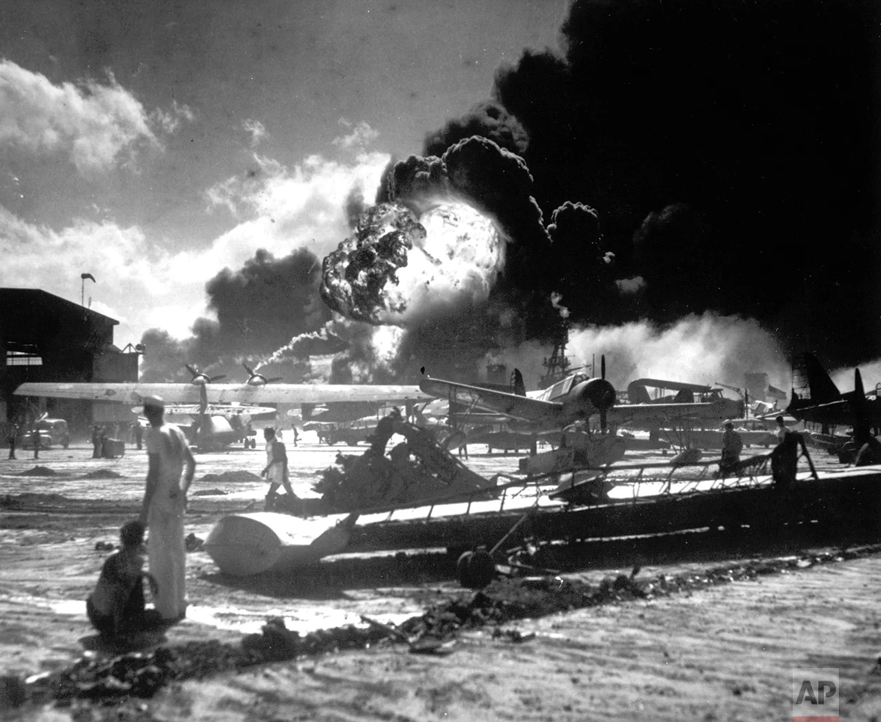 In this image provided by the U.S. Navy, sailors stand among wrecked airplanes at Ford Island Naval Air Station as they watch the explosion of the USS Shaw in the background, during the Japanese surprise attack on Pearl Harbor, Hawaii, on December 7, 1941. (AP Photo/U.S. Navy)