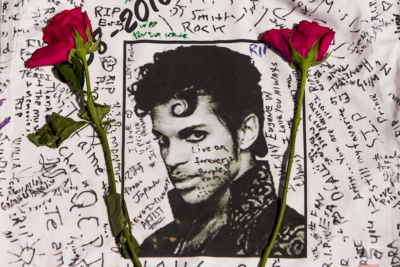  Flowers lie on a T-shirt signed by fans of singer Prince at a makeshift memorial place created outside the Apollo Theater in New York on April 22, 2016. The pop star died at the age of 57. (AP Photo/Andres Kudacki) 