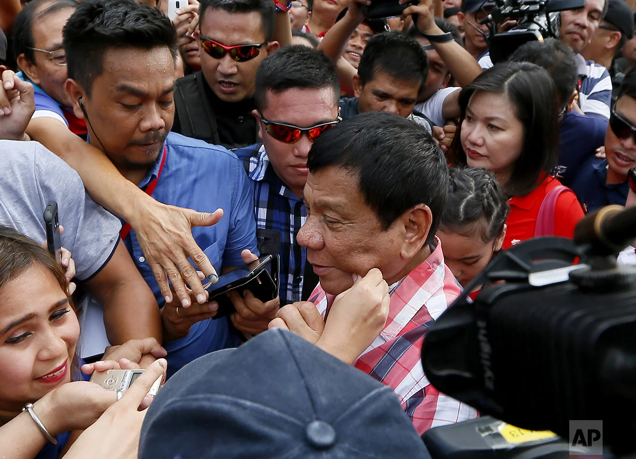 A supporter pinches the cheek of front-running presidential candidate Mayor Rodrigo Duterte as he leaves Daniel R. Aguinaldo National High School at Matina district, his hometown, after voting in Davao city in southern Philippines on May 9, 2016. (AP Photo/Bullit Marquez)