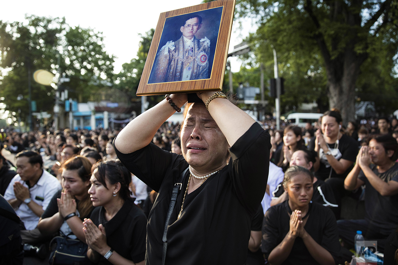  A Thai woman cries as she holds a picture of the late King Bhumibol Adulyadej while others clasp their hands to pay last respects to a passing van carrying the body of their king outside the Grand Palace in Bangkok, Thailand, on Oct. 14, 2016. Bhumi