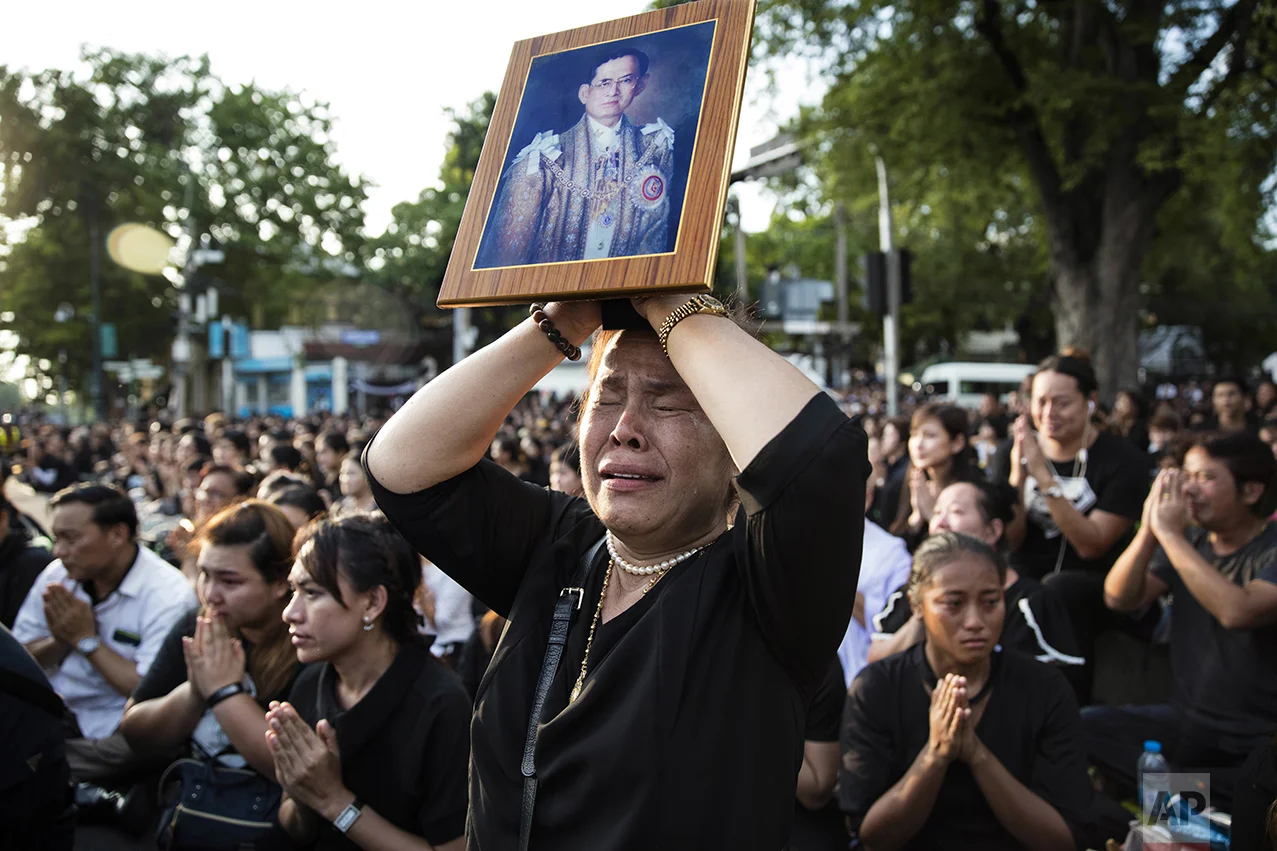 A Thai woman cries as she holds a picture of the late King Bhumibol Adulyadej while others clasp their hands to pay last respects to a passing van carrying the body of their king outside the Grand Palace in Bangkok, Thailand, on Oct. 14, 2016. Bhumibol, the world's longest reigning monarch, died at the age of 88. (AP Photo/Wason Wanichakorn)