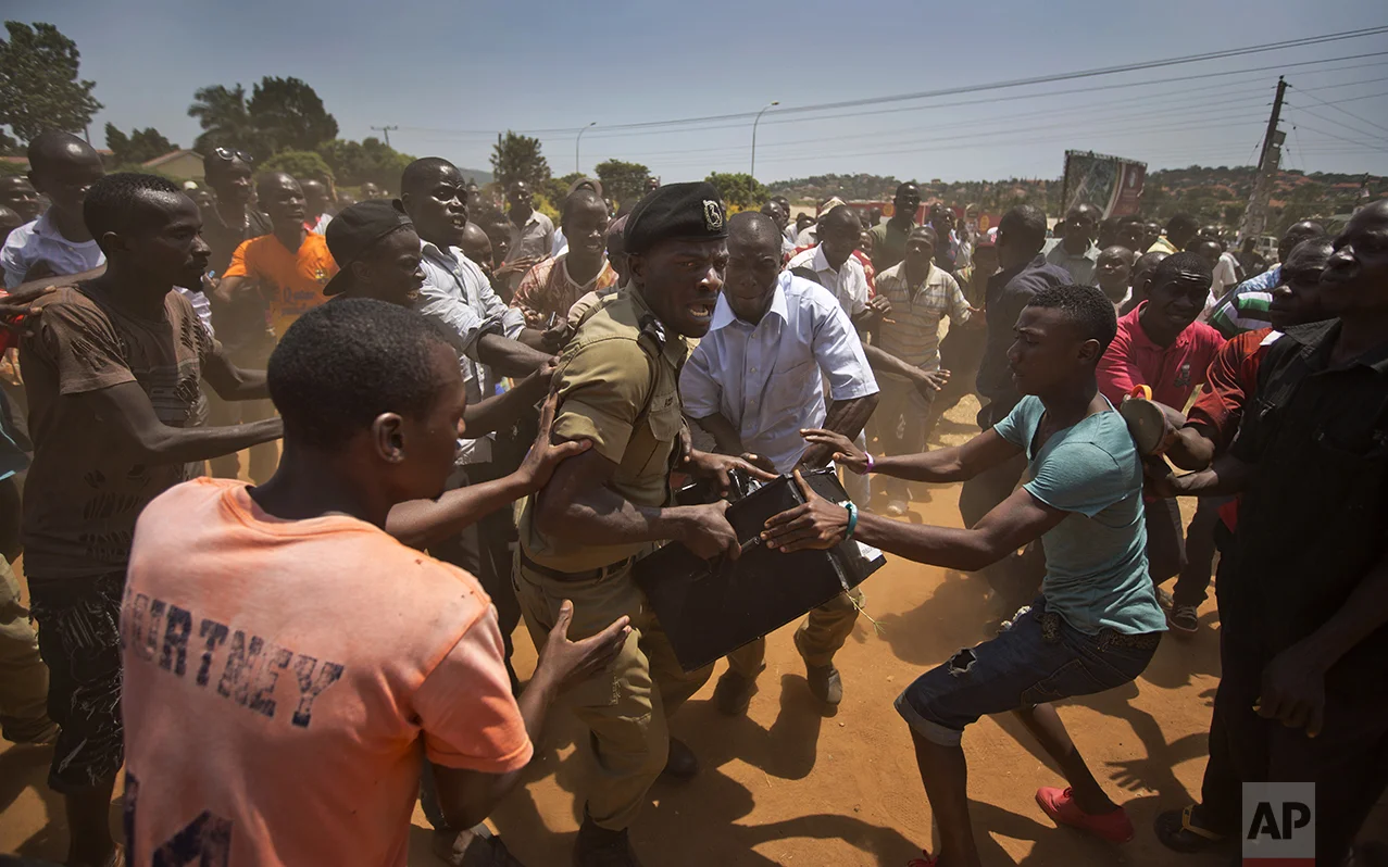 A Ugandan policeman struggles to keep hold of a box containing voting material as excited voters surround him after waiting over 7 hours without being able to vote, at a polling station in Ggaba, on the outskirts of Kampala, Uganda, on Feb. 18, 2016. (AP Photo/Ben Curtis)