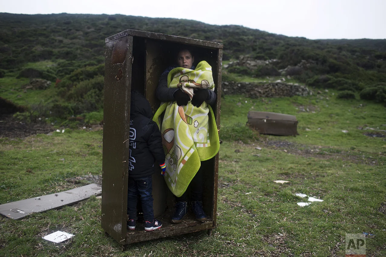 A Syrian woman takes shelter with her children in an iron box during a rainfall after they arrived from Turkey to the Greek deserted island of Pasas near Chios, on Jan. 20, 2016. Thousands of migrants and refugees continue to reach Greece's shores despite the winter weather. (AP Photo/Petros Giannakouris)