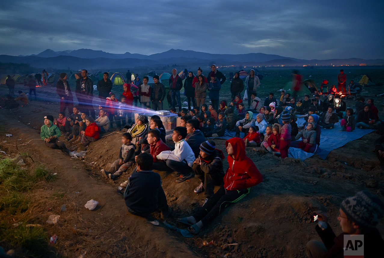  Children watch an animated movie in a field at the northern Greek border station of Idomeni on March 5, 2016. The Idomeni border crossing in the Greek region of Central Macedonia has become a bottleneck, where thousands of migrants are trapped as th