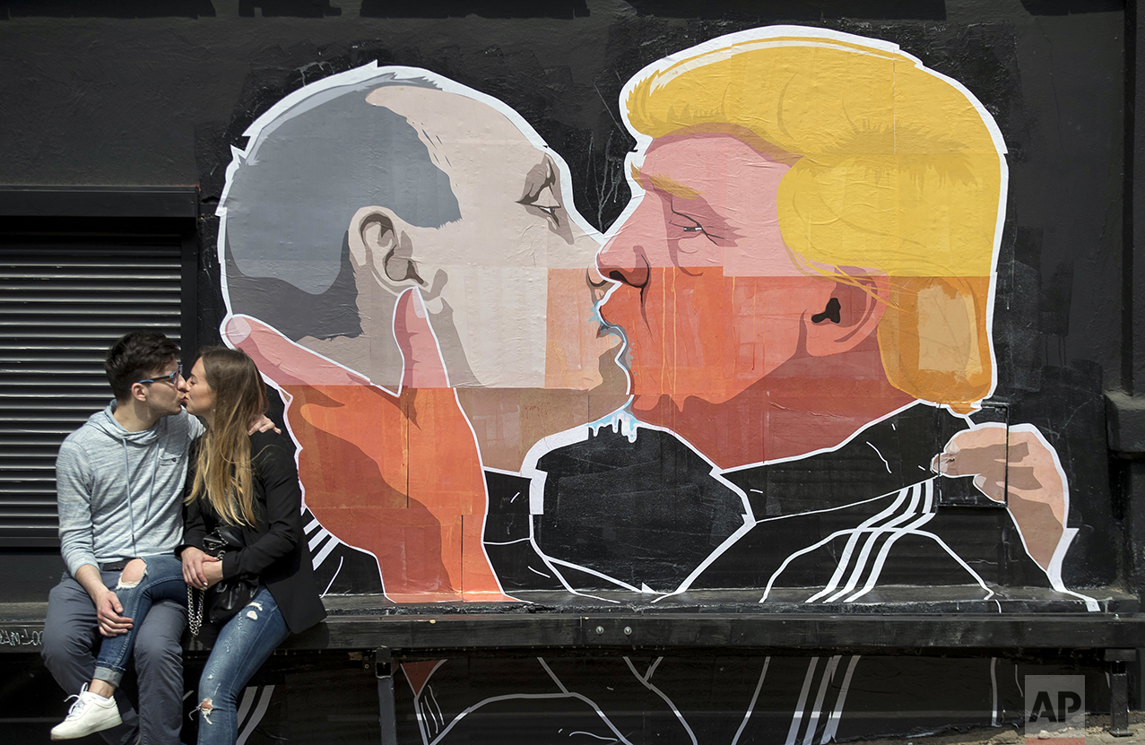 A couple kisses in front of graffiti depicting Russian President Vladimir Putin, left, and Republican presidential candidate Donald Trump, on the walls of a bar in the old town in Vilnius, Lithuania, on May 14, 2016. (AP Photo/Mindaugas Kulbis)