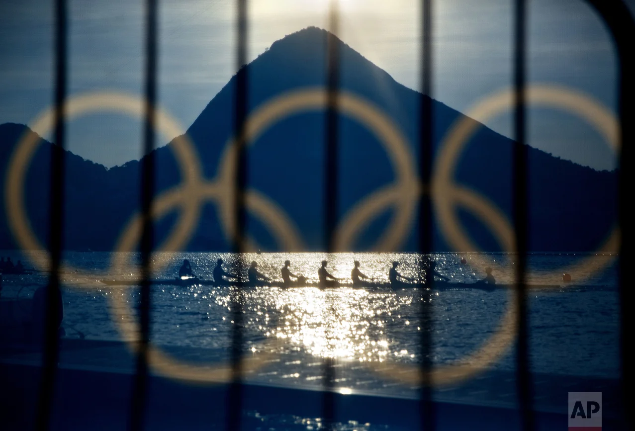 Rowers are seen through a screen decorated with the Olympic rings as they practice at the rowing venue in Lagoa at the 2016 Summer Olympics in Rio de Janeiro, Brazil, on Aug. 7, 2016. (AP Photo/David Goldman)