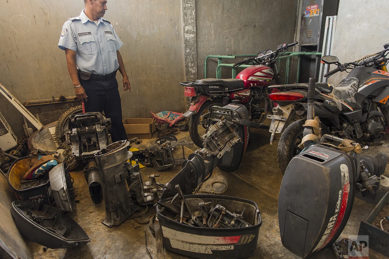 In this Nov. 11, 2016 photo, a municipal police officer stands amid stolen engines seized from pirates, at the police station in Punta de Araya, Sucre state, Venezuela. "People can't make a living fishing anymore, so they're using their boats for the options that are left: smuggling gas, running drugs, and piracy," said Jose Antonio Garcia, leader of the state's largest union. (AP Photo/Rodrigo Abd)