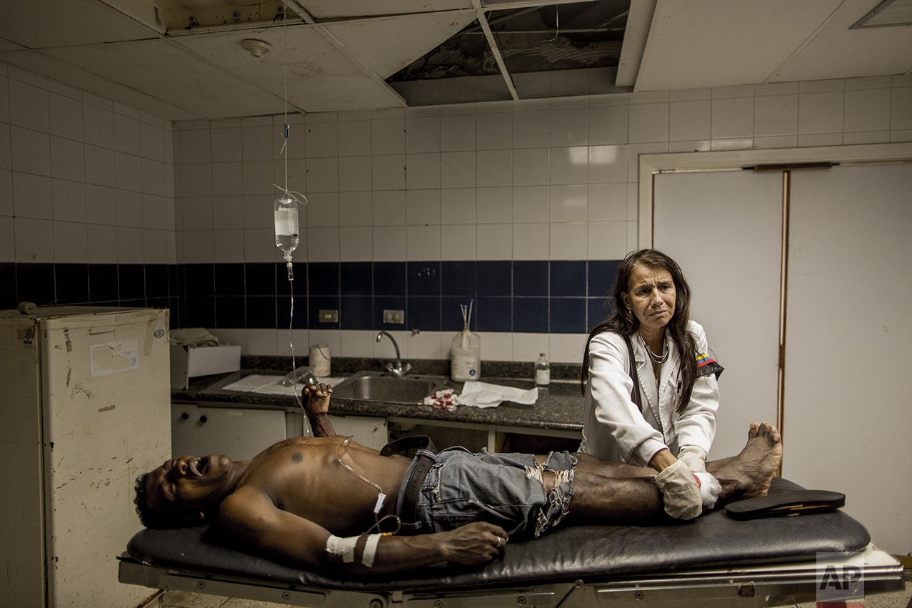 In this Nov. 3, 2016 photo, lead emergency room doctor Norka Patino treats a man who was shot in Cumana, Sucre state, Venezuela. Patino, who's been working at the hospital for over 20 years, said she has to use the same needle on various patients and that many die unnecessarily of heart attacks, diarrhea, asthma and from bacterias picked up at the hospital. The band on her arm is the Venezuelan flag accented with a black band to protest her hospital's lack of basic supplies. (AP Photo/Rodrigo Abd)