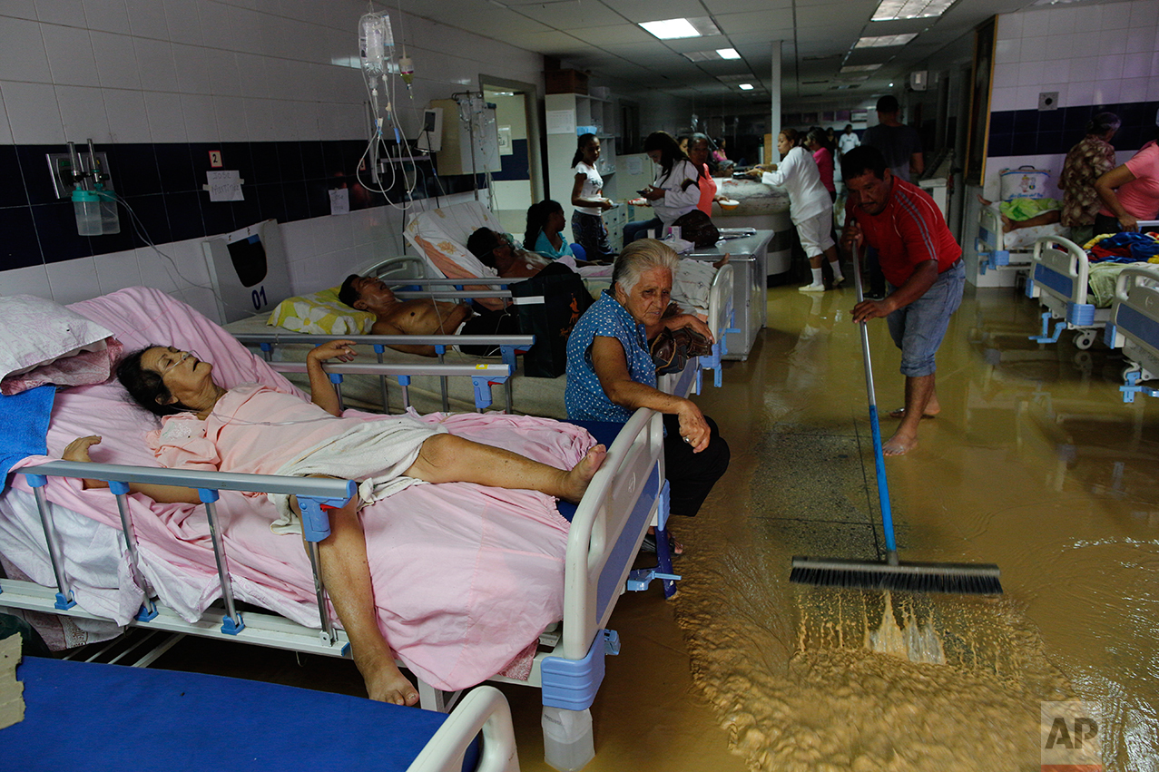 In this Nov. 3, 2016 photo, the relative of a public hospital patient pushes water out of the emergency room after flooding triggered by heavy rain in Cumana, Sucre state, Venezuela. The hospital lacks medicine and beds. Hygiene is so bad that some patients who come to the ER end up dying from bacterial infections caught there. (AP Photo/Rodrigo Abd)