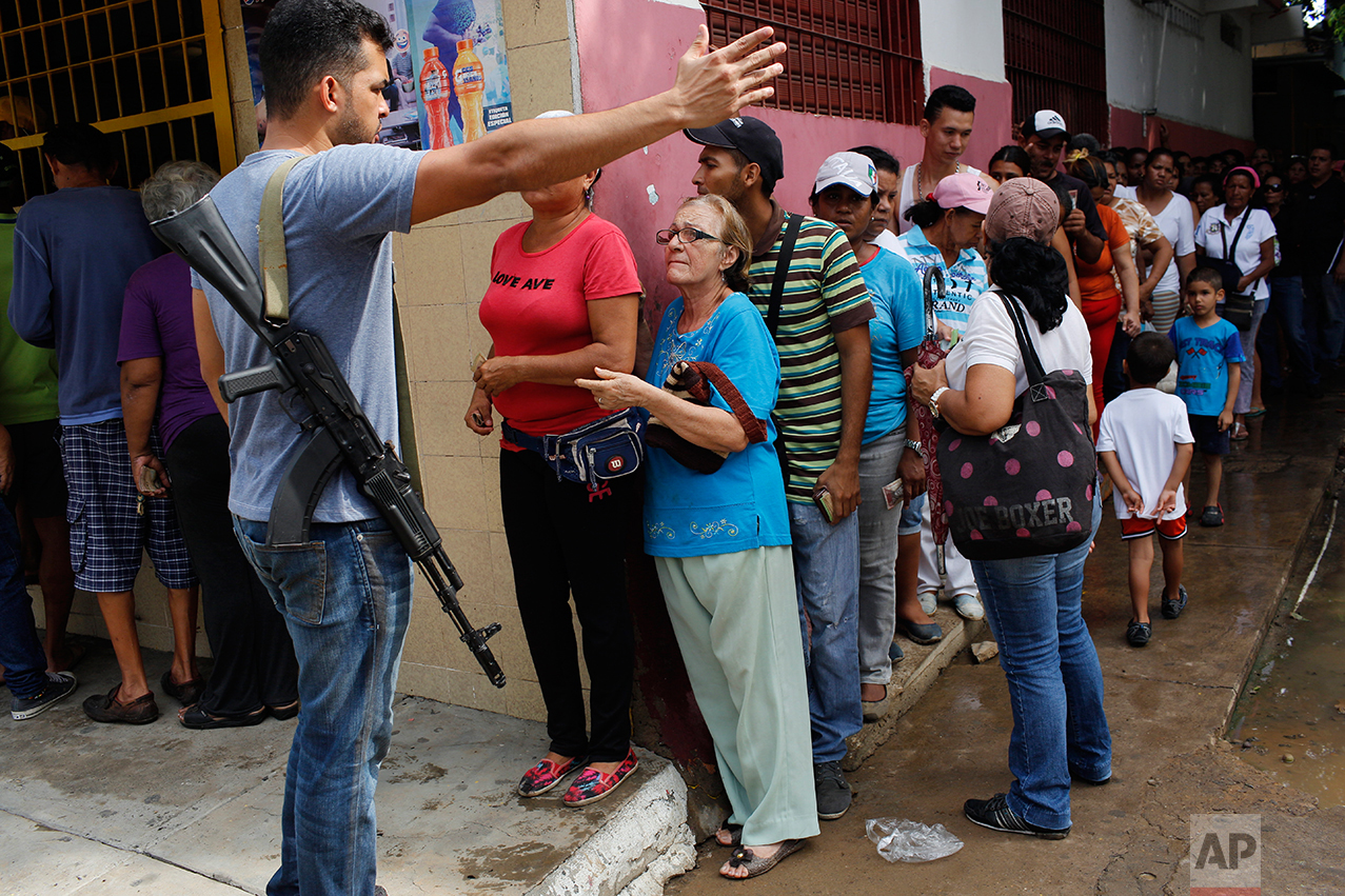 In this Nov. 4, 2016 photo, a security officer from the anti-extortion and kidnapping command of the National Guard (CONAS), gives instructions to residents lining up to buy food at a store in downtown Cumana, Sucre state, Venezuela. CONAS agents provide security for arriving food trucks after the state became the epicenter of food riots that swept through the country over the summer. (AP Photo/Rodrigo Abd)