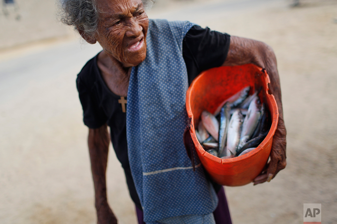 In this Nov. 14, 2016 photo, a woman carries a bucket of fish that her fishermen neighbors gave her as a gift as she returns home from work in Punta de Araya, Sucre state, Venezuela. When times are hard, Venezuela's capital city gets the lion's share of resources and the provinces get less than ever. (AP Photo/Rodrigo Abd)