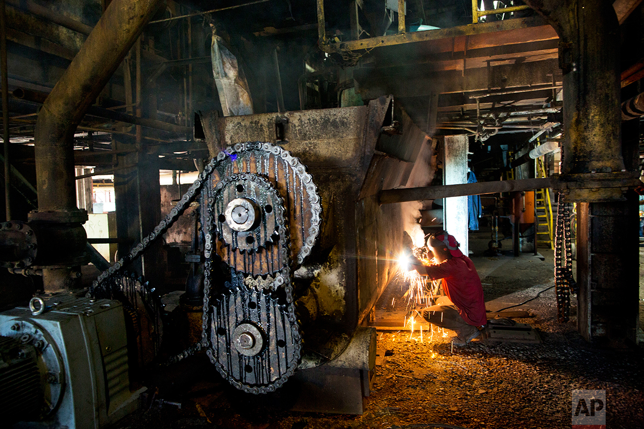 In this Nov. 3, 2016 photo, a worker repairs machinery to get it ready for the next sugar cane harvest at a sugar mill in Cumanacoa, Sucre state, Venezuela. "We are revolutionaries, but in this factory there are no letters of credit, no spare parts for the machines, so we do what we can to keep it going," said welder Jose Armando Bastardo. (AP Photo/Rodrigo Abd)