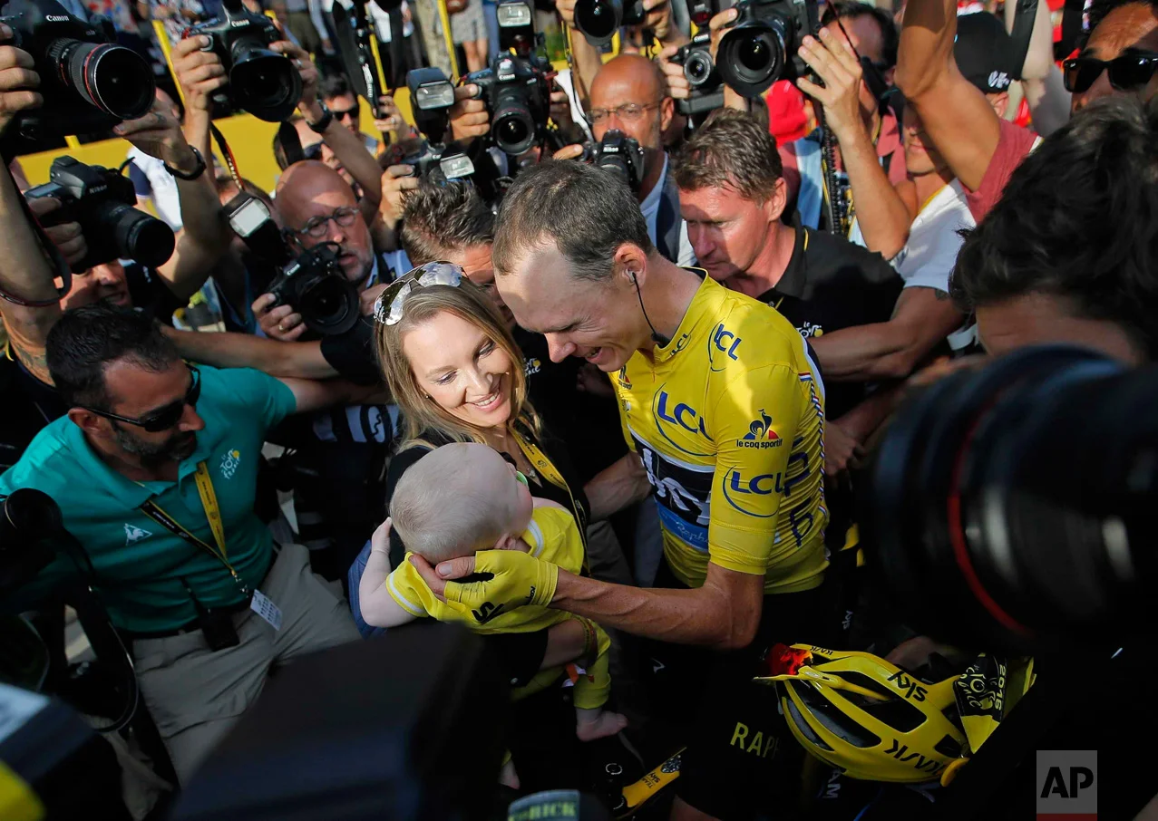 In this Sunday, July 24, 2016 photo, Tour de France champion, Britain's Chris Froome, wearing the overall leaders yellow jersey, is congratulated by his wife Michelle, who holds their baby boy, after the twenty-first stage of the Tour de France cycling race over 113 kilometers (70.2 miles) with start in Chantilly and finish in Paris, France. (AP Photo/Christophe Ena)