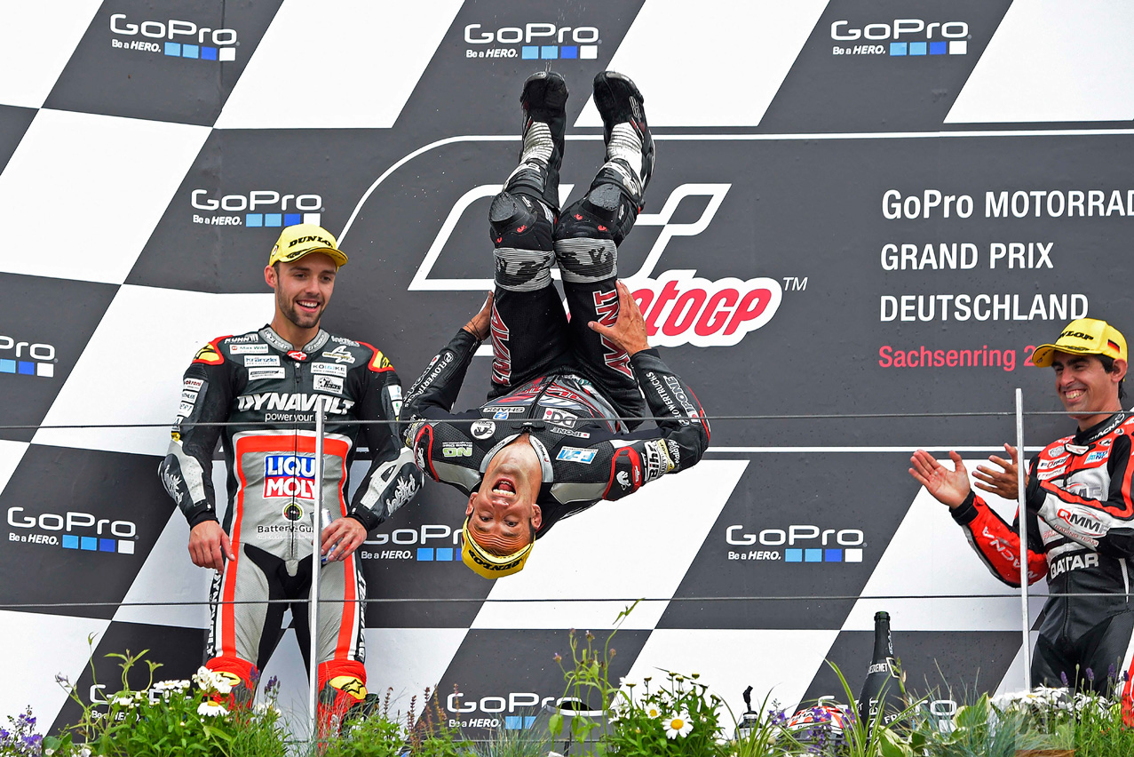  In this Sunday, July 17, 2016 photo, second placed driver Jonas Folger, left, from Germany and third placed Julian Simon, right, from Spain look on as first placed Moto 2 driver Johann Zarco, center, from France performs a backflip during the award 