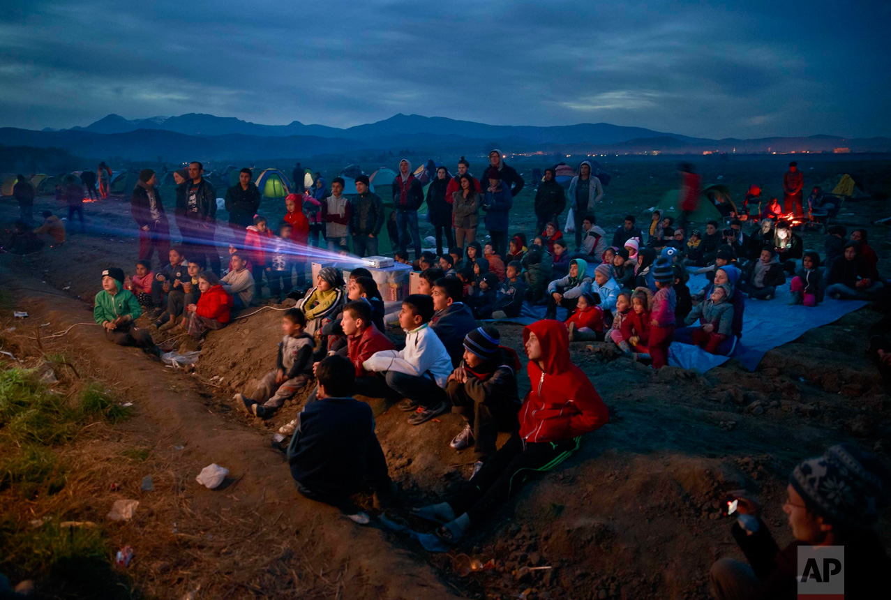  In this March 5, 2016 photo, children watch an animated movie in a field at the northern Greek border station of Idomeni. The Idomeni border crossing in the Greek region of Central Macedonia has become a bottleneck, where thousands of migrants are t