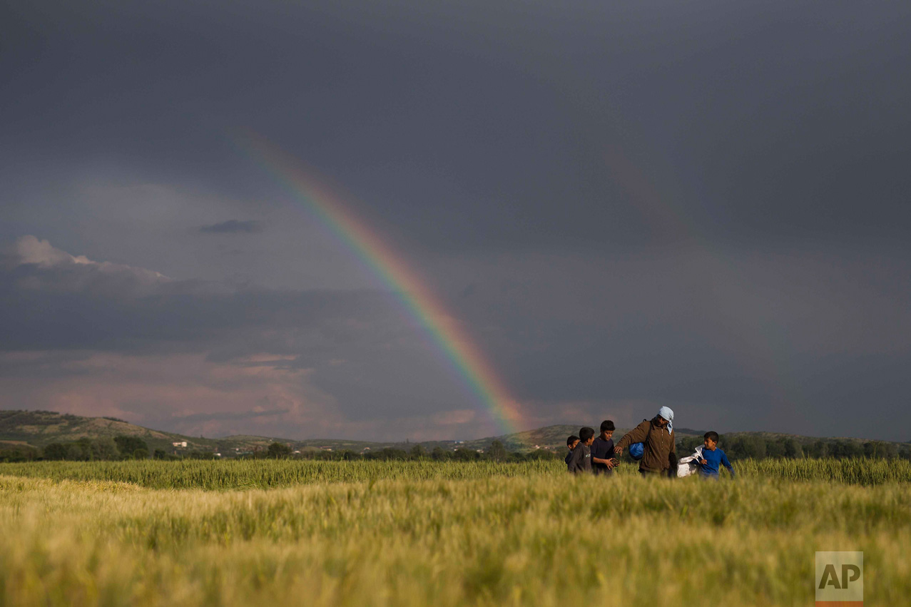  In this Saturday, May 7, 2016 photo, Syrian refugees walk on fields in front of a rainbow at the northern Greek border point of Idomeni, Greece. Thousands of migrants and refugees are trapped in Idomeni for months unable to continue their trip to Eu