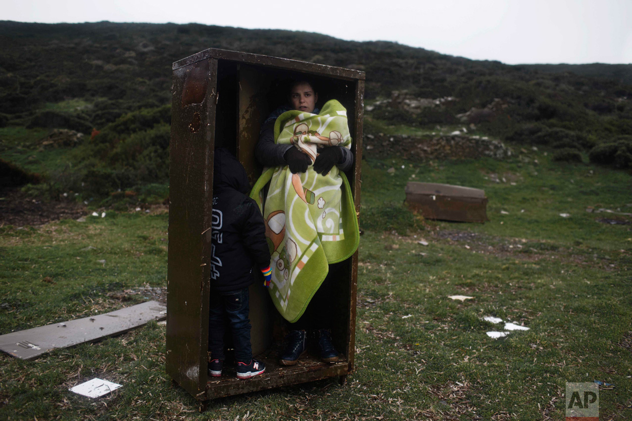  In this Wednesday, Jan. 20, 2016 photo, a Syrian woman with her children takes a shelter in a iron box during a rainfall after they arrived from Turkey to the Greek deserted island of Pasas near Chios. Europe's biggest migration crisis since the end