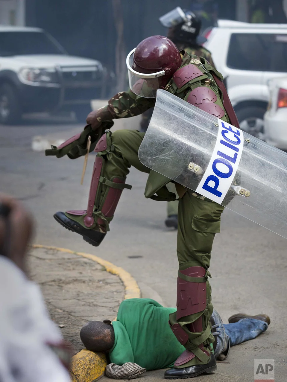 In this Monday, May 16, 2016 photo, a Kenyan riot policeman repeatedly kicks a protester as he lies in the street after tripping over while trying to flee from them, during a protest in downtown Nairobi, Kenya. Kenyan police have tear-gassed and beaten opposition supporters during a protest demanding the disbandment of the electoral authority over alleged bias and corruption. (AP Photo/Ben Curtis)