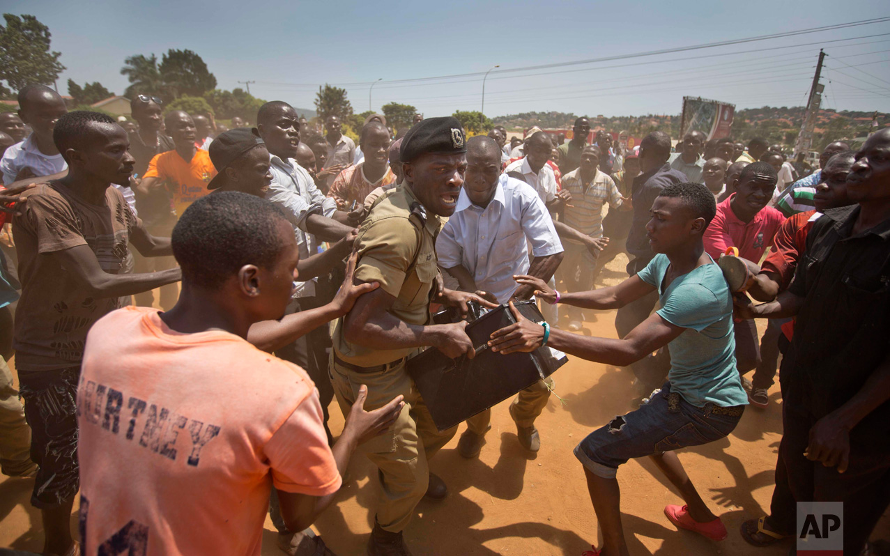  In this Thursday, Feb. 18, 2016 photo, a Ugandan policeman struggles to keep hold of a box containing voting material, as excited voters surround him after waiting over 7 hours without being able to vote, at a polling station in Ggaba, on the outski