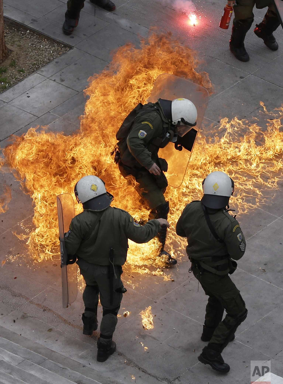  In this Thursday, Feb. 4, 2016 photo, riot policemen try to avoid a petrol bomb thrown by protesters during a 24-hour nationwide general strike in Athens. Clashes have broken out between Greek police and youths throwing fire bombs and stones, as ten