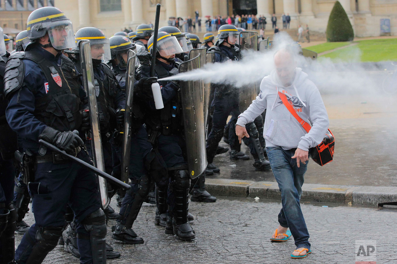  In this Thursday, May 12, 2016 photo, French riot police officers spray pepper gas at a demonstrator during a protest against Labor Law as the Socialist government decided to force the bill through Parliament without a vote, in Paris. France's gover