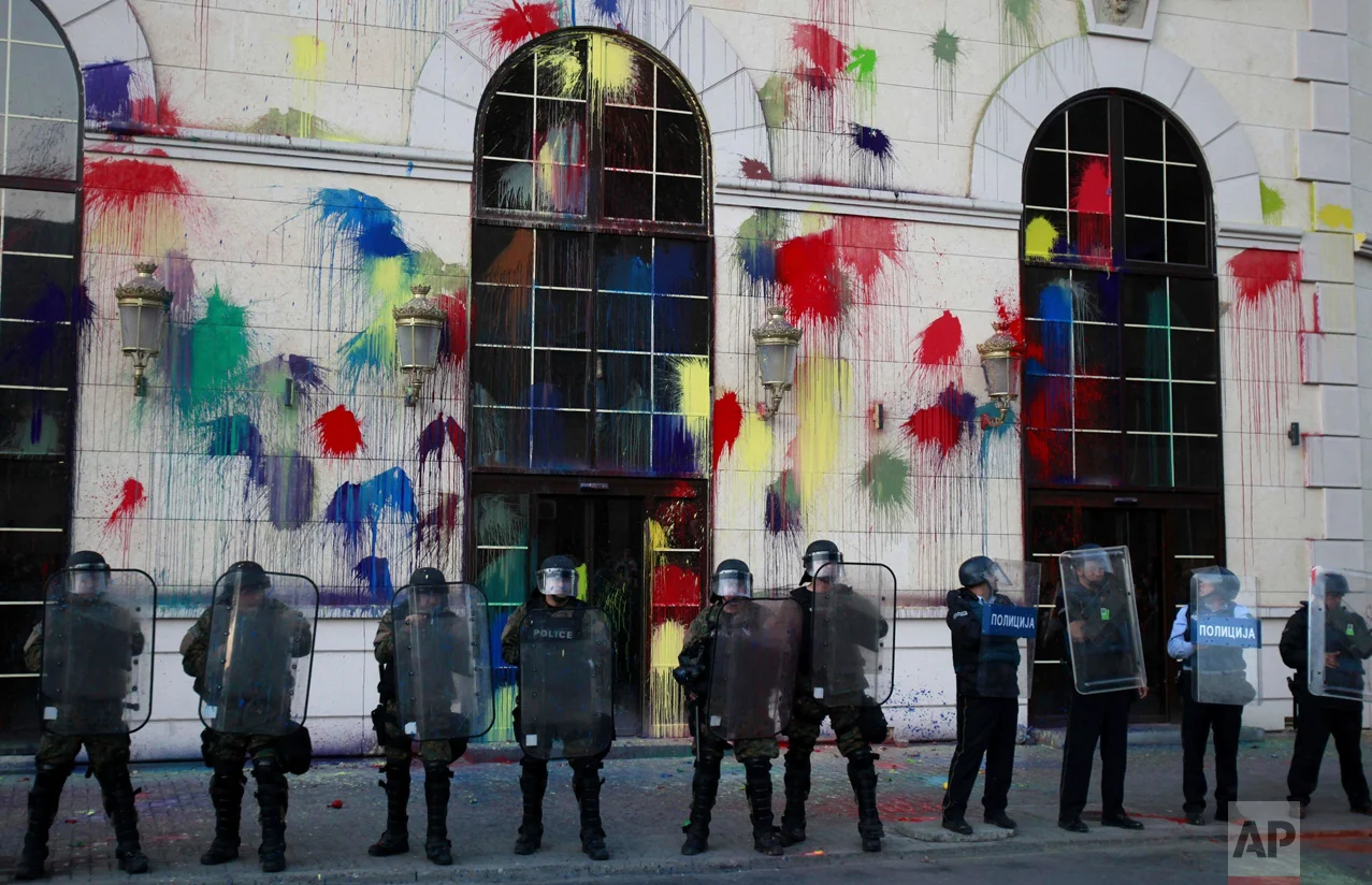 In this Friday, April 22, 2016 photo, police officers hold their shields as protestors pelt the new building of the Agency for Media Services with colored paint, during a protest in Skopje, Macedonia. Thousands of people have been protesting almost nightly in the Macedonian capital, Skopje, since President Gjorge Ivanov announced a decision last week to grant presidential pardons that halted criminal proceedings against dozens of people, including high-ranking politicians, accused in a wiretapping scandal that has roiled Macedonia for months. (AP Photo/Boris Grdanoski)
