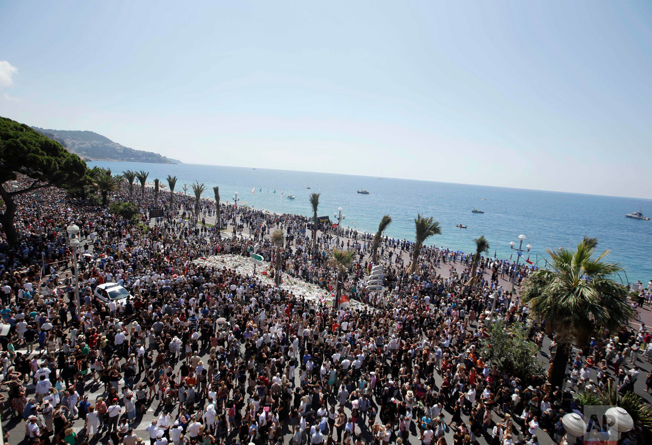  In this Monday, July 18, 2016 photo, people gather at a makeshift memorial to observe a minute of silence to honor the victims of an attack near the area where a truck mowed through revelers on the famed Promenade des Anglais in Nice, southern Franc