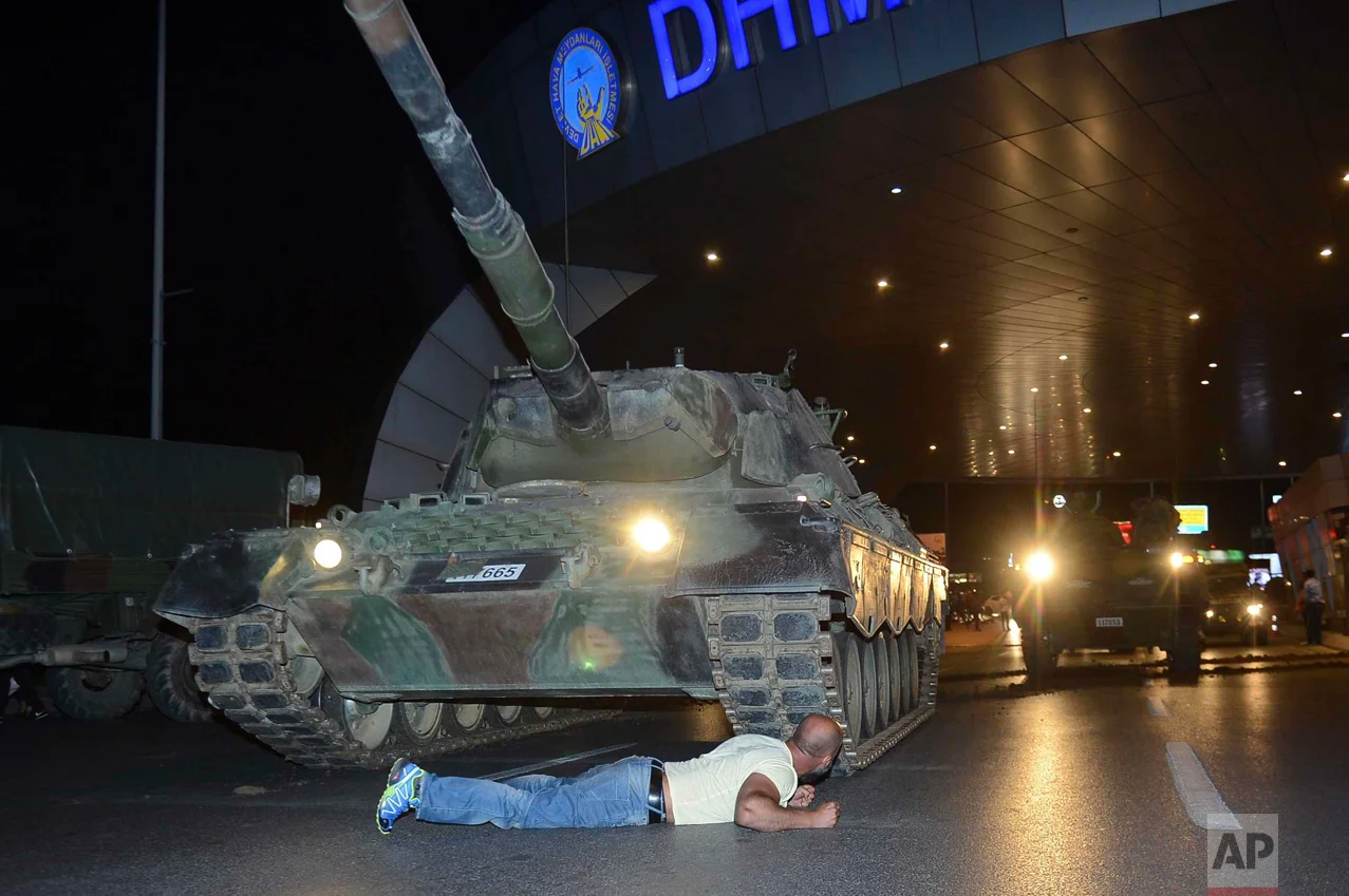 In this Saturday, July 16, 2016 photo, a man lays in front of a tank in the entrance to Istanbul's Ataturk airport. Members of Turkey's armed forces said they had taken control of the country, but Turkish officials said the coup attempt had been repelled early Saturday morning in a night of violence that left several people dead, according to state-run media. (Ismail Coskun/IHA via AP)