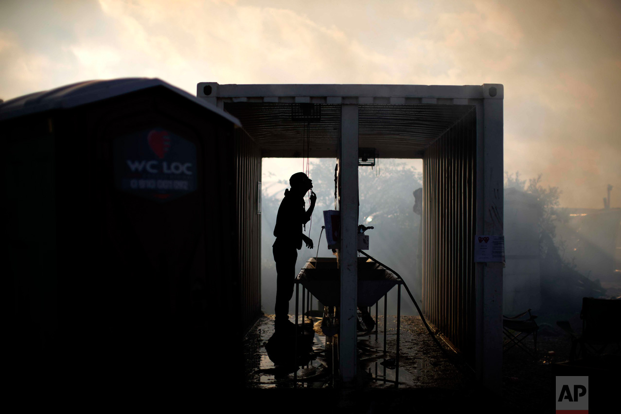  In this Thursday, Oct. 27, 2016 photo, a migrant shaves himself amid of smoke provoked by tents burning as workers clean-up a makeshift migrant camp known as "the jungle" near Calais, northern France. (AP Photo/Emilio Morenatti) 