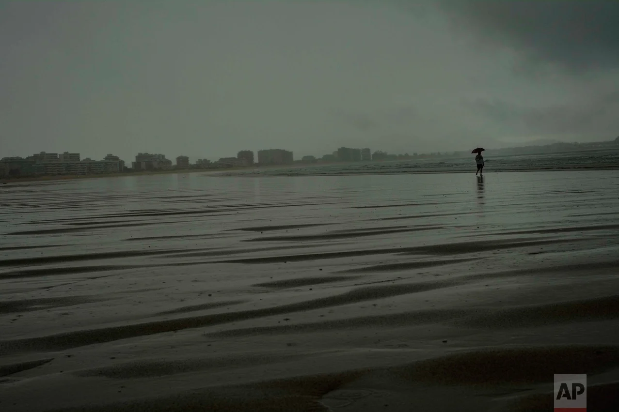 In this Saturday, July 30, 2016 photo, a man shelters from the rain with an umbrella as he goes for a walk on the seaside during a rainier summer day, in Laredo, northern Spain. (AP Photo/Alvaro Barrientos)