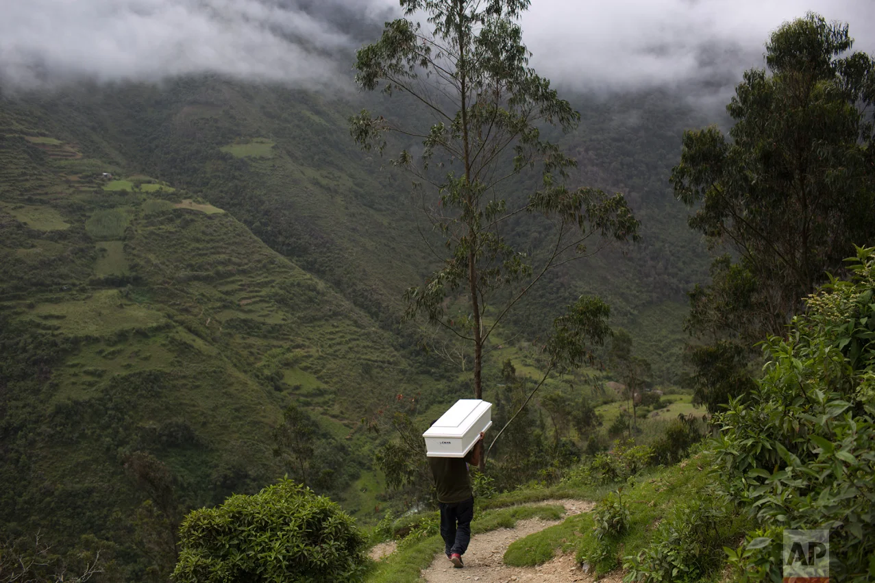 In this March 29, 2016 photo, a man shoulders a coffin with the remains of a loved one, who was slain more than two decades ago by Shining Path guerrillas, while walking to the cemetery for a mass burial service, in Huanta, Peru. The remains of 40 victims were returned to their loved ones in a ceremony supported by the International Red Cross. (AP Photo/Rodrigo Abd)