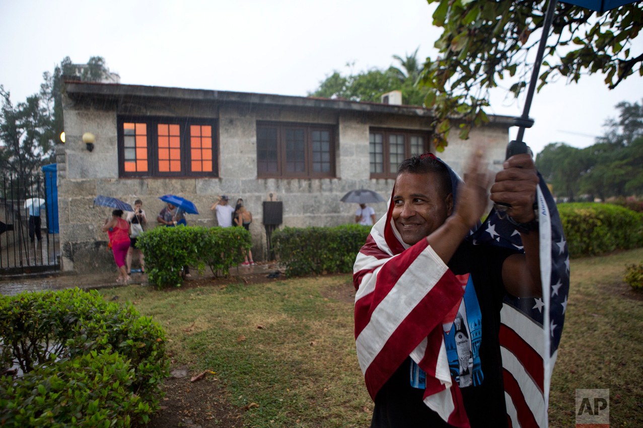  In this March 20, 2016 photo, a Cuban wearing a U.S. national flag applauds as President Barack Obama's convoy passes by in the rain along the Malecon into Old Havana, Cuba. Obama's trip to the island nation was a crowning moment in his and Cuban Pr