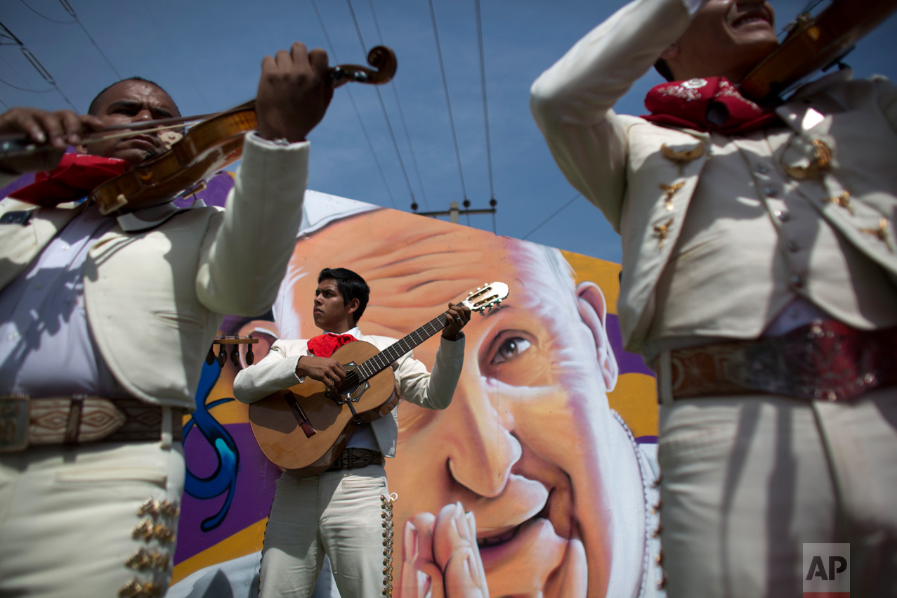  In this Feb. 14, 2016 photo, mariachis backdropped by a mural depicting Pope Francis, as they wait for the popemobile to pass following the end of a Mass, in Ecatepec, Mexico. Francis condemned the drug trade's "dealers of death" and urged Mexicans 