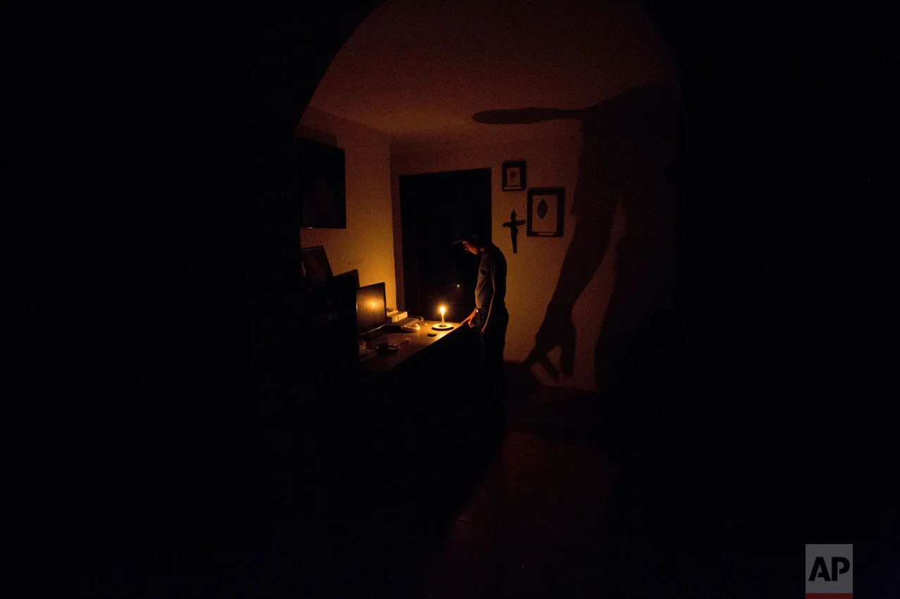 In this April 23, 2016 photo, a boy illuminates his home with a candle during a 24-hour blackout, in the El Calvario neighborhood of El Hatillo, just outside of Caracas, Venezuela. Energy rationing was added to the hardships faced by Venezuelans overwhelmed by inflation, shortages of food and medicine, and rising crime. (AP Photo/Fernando Llano)