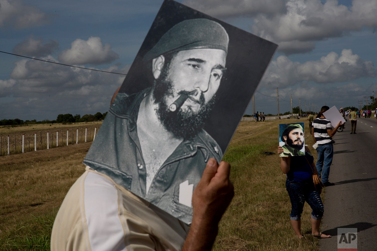  In this Dec. 2, 2016 photo, a man uses an image of Fidel Castro to shade himself from the sun while waiting for the convoy carrying the ashes of Cuba's late leader, along the central road near Yarigua, Las Tunas, Cuba. The convoy traced in reverse t