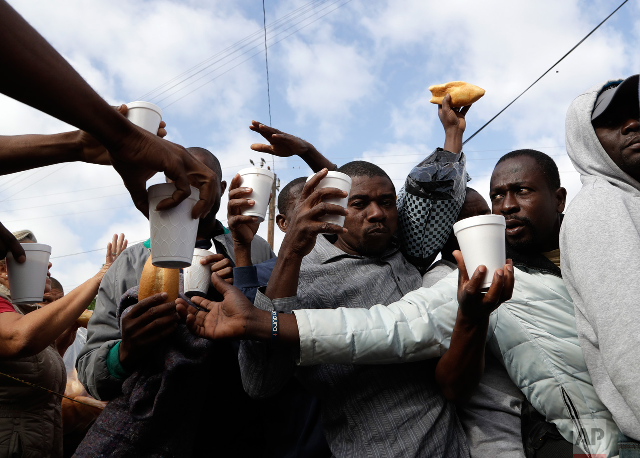  In this Oct. 3, 2016 photo, Haitian migrants receive food and drinks from volunteers as they wait in line at a Mexican immigration agency with the hope of gaining an appointment to cross into the U.S., in Tijuana, Mexico. A surge in border crossings