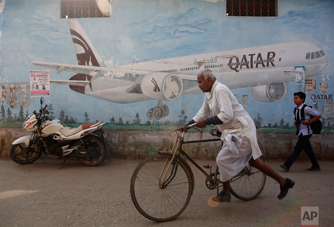 In this photo taken on Monday, Nov. 30, 2016, a Nepalese man rides his bicycle in front of an advertisement of Qatar airways painted on a wall in Janakpur district, Nepal. The number of Nepali workers going abroad has more than doubled since the country began promoting foreign labor in recent years: from about 220,000 in 2008 to about 500,000 in 2015. The unskilled workers fill a host of global demands: building highways, stadiums and houses in Gulf states and guarding shopping malls, sewing sweatshirts and assembling televisions in Malaysia. (AP Photo/Niranjan Shrestha)