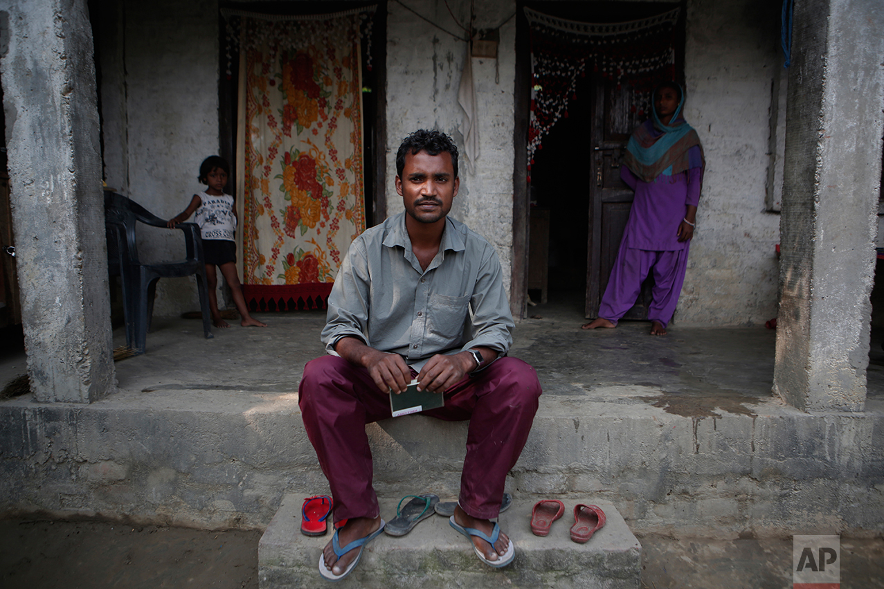In this Nov. 23, 2016 photo, Mohammed Tohit, 28, holds his passport in front of the solid, cement and plaster home that he built for his family in Belhi Village, Nepal. Tohit is the envy and inspiration of the village. He worked in Malaysia for almost six years sewing clothes for Nike, Lacoste and Columbia Sportswear, saving more than $20,000, enough to build the sturdy two-bedroom house. "I am scared, sure, but I have no way to earn anything here," he says. "I have no choice but to leave again." (AP Photo/Niranjan Shrestha)