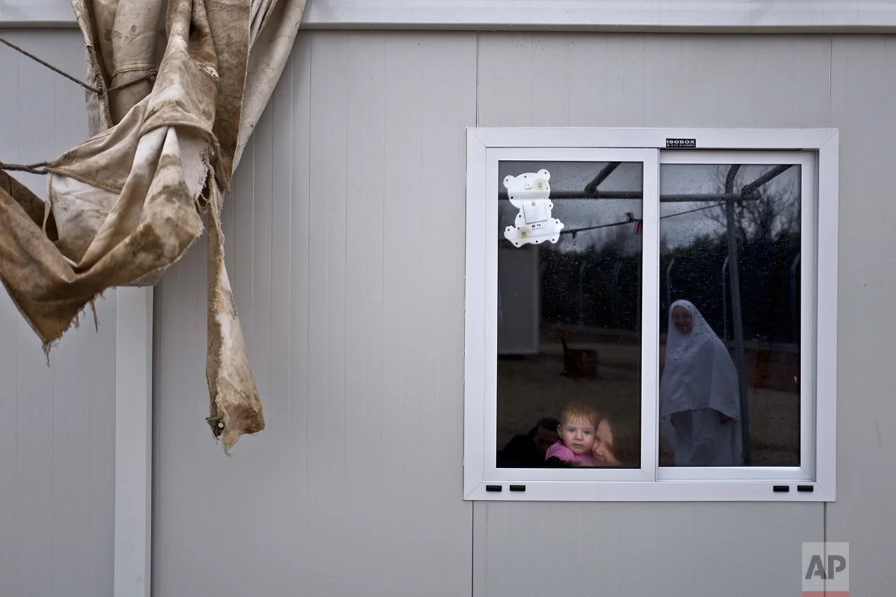 Syrian refugee Raneen Mahmoud, 5, and her younger sister Zainab, 6 months, look at their mother Randa, 30, from their shelter at the refugee camp of Ritsona about 86 kilometers (53 miles) north of Athens, Wednesday, Dec. 28, 2016. (AP Photo/Muhammed Muheisen)