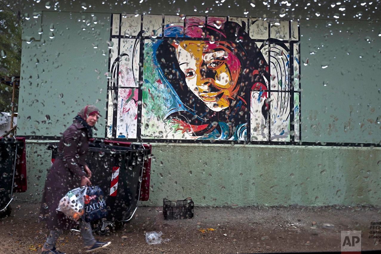 A Syrian refugee woman walks back to her shelter carrying bags of food at the refugee camp of Ritsona about 86 kilometers (53 miles) north of Athens, Wednesday, Dec. 28, 2016. (AP Photo/Muhammed Muheisen)